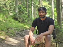 Goutham in the forest, sitting on a tree stump.
