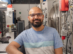Male person with glasses and beard, wearing a blue and white striped t-shirt inside one at the experimental caves at the Centre for Advanced Laser Applications (CALA)